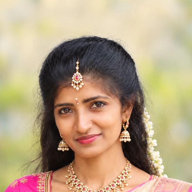 Illustration of Sindhu smiling, in a cream and magenta silk saree with a maang tikka, jhumka earrings and a jasmine garland